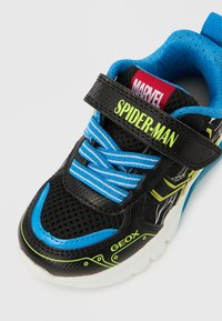 Czarny sneaker z niebieskimi akcentami, siateczkową cholewką oraz neonowozielonym napisem "SPIDER-MAN" na pasku; wyposażony w logo Geox i teksturowane podeszwy.