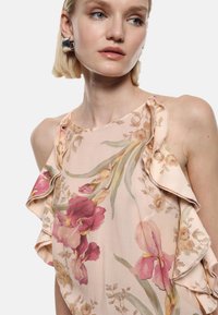 Top floreale a balze in morbido tessuto rosa, con grandi stampe di fiori viola e gialli. Progettato con una forma fluida e delicate balze.
