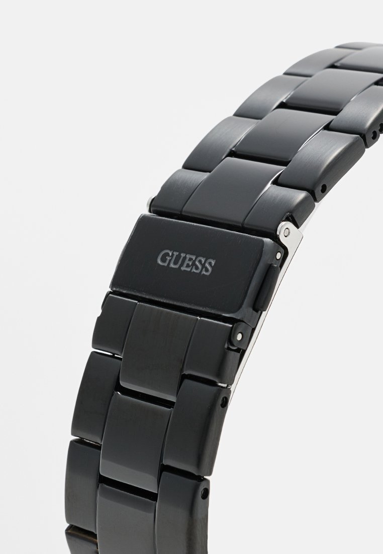 Reloj de pulsera de metal negro con diseño de pulsera de eslabones. Cuenta con un acabado pulido y el logo "GUESS" grabado en el cierre. Textura suave en toda la superficie.