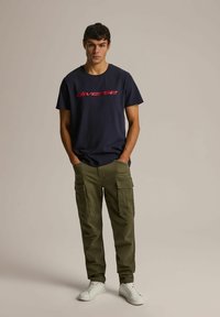 Granatowa bawełniana koszulka z czerwonym napisem "diverse", zestawiona z oliwkowymi spodniami cargo z bocznymi kieszeniami i białymi sneakersami.