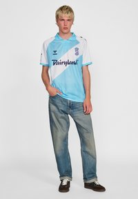 Vit och ljusblå pikétröja med diagonal ljusblå rand, "Dairyland"-logotyp; bärs med lösa blå jeans och mörka skor.
