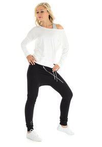 White long-sleeve top with an off-shoulder design paired with black jogger pants featuring zippered pockets, styled with white sneakers.