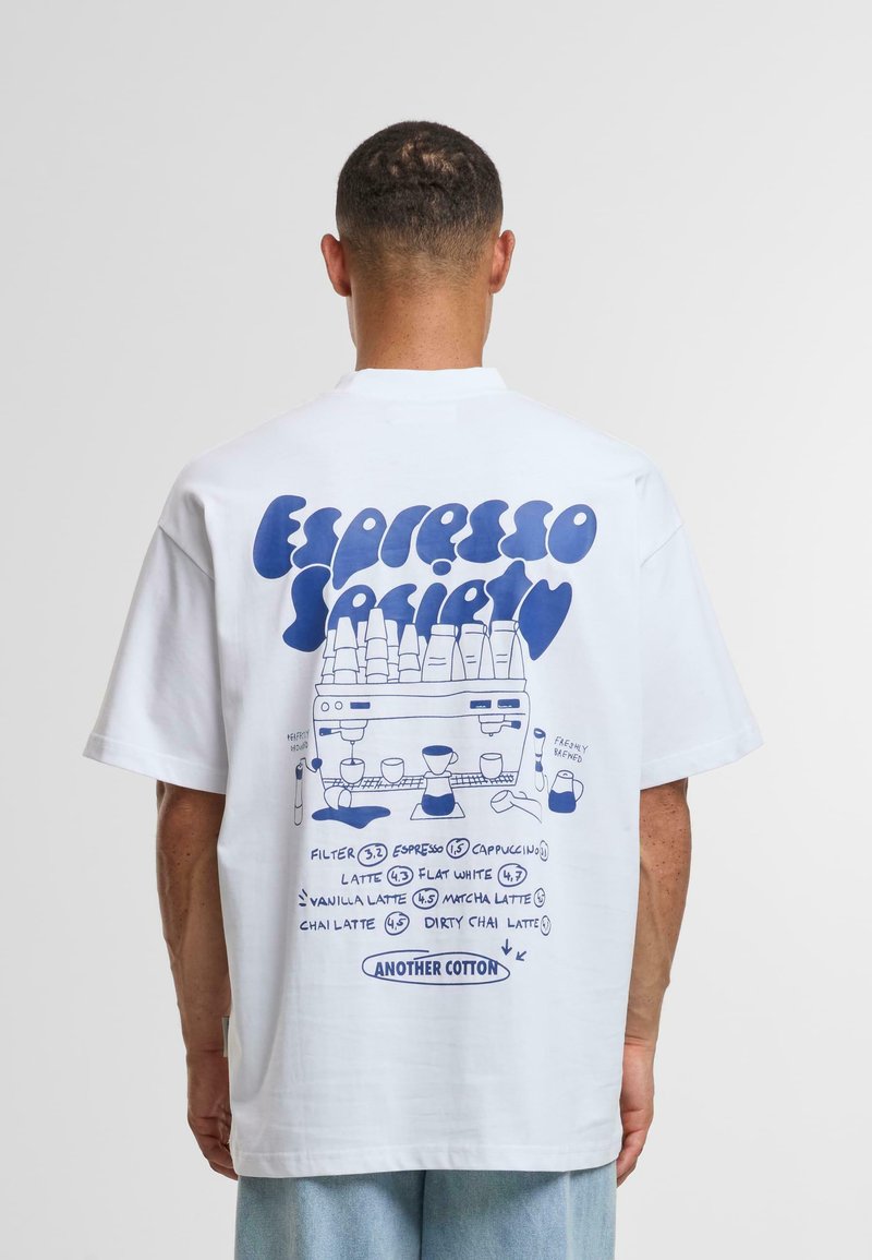 Camiseta de algodón blanca con un diseño gráfico azul en la parte posterior, que representa varias bebidas de café y una ilustración de una máquina de café.