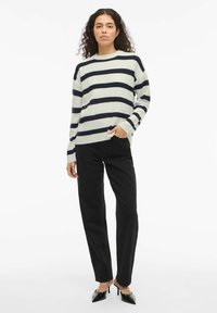 Pull en maille rayé crème et marine, coupe décontractée, texture côtelée, col rond. Associé à un jean droit noir et des talons pointus.