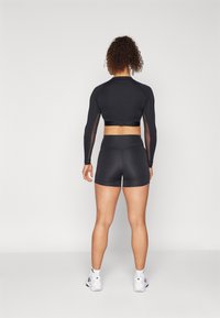 Top sportivo nero aderente con maniche lunghe e dettagli in rete abbinato a pantaloni corti neri a vita alta. Texture liscia, design aderente.