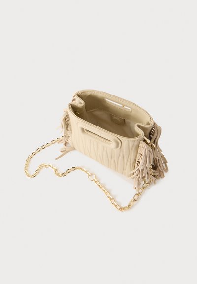 Sac à main matelassé beige avec franges sur les côtés et bandoulière chaîne dorée, présenté ouvert et vide sur un fond clair uni.