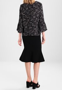 Flowy black top with white floral pattern and bell sleeves, paired with a black fitted skirt featuring a flared hem; worn with black heels.
