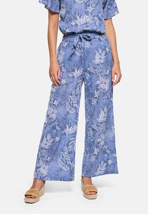 Pantalones anchos azules con estampados de hojas tropicales blancas, cintura anudada, combinados con sandalias de cuña tejidas.