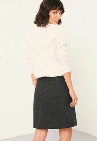 Cremefarbenes, strukturiertes Sweatshirt mit langen Ärmeln, kombiniert mit einem knielangen, dunkelgrauen Bleistiftrock mit dezenten Mustern und einem Reißverschluss auf der Rückseite.