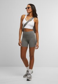 Sujetador deportivo blanco cortado con diseño de recortes, pantalones cortos gris de cintura alta y zapatillas gris con acentos blancos. El modelo también lleva gafas de sol y un bolso.