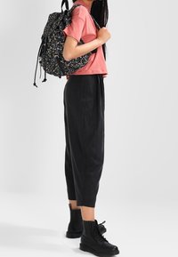 Sac à dos noir à motif floral, chemise rose à manches courtes, pantalon noir fuselé, bottes noires à lacets. Caractéristiques : bretelles réglables et détails zippés.