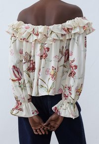 Blouse à épaules dénudées en tissu léger à motif floral. Encolure et poignets à volants, coupe ample avec un design plissé.
