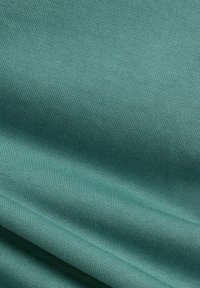 Matériau textile, texture douce, dans une couleur teal atténuée. Le tissu présente un motif à côtes fines avec un léger éclat, tombant délicatement.