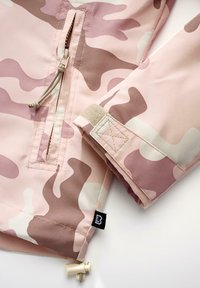 Lengva rožinė maskuojanti striukė su rudos ir kreminės spalvos raštais, turinti priekinę užtrauktuką, reguliuojamą raištelį su užsegimais ir Velcro užsegimą rankogaliuose.