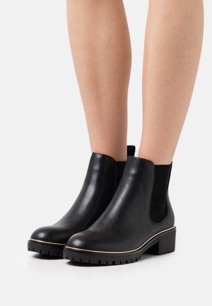Black leather ankle boots with elastic side panels, rounded toe, and low block heel. Features a textured sole with grooves and subtle gold trim.