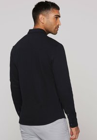Navy long-sleeve shirt with a textured surface, button cuffs, and a collar. Features back yoke seam and curved hemline.