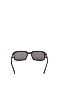 Svarta rektangulära solglasögon med mörka linser, tunna guldiga detaljer längs den övre kanten och släta, raka svarta skalmar.