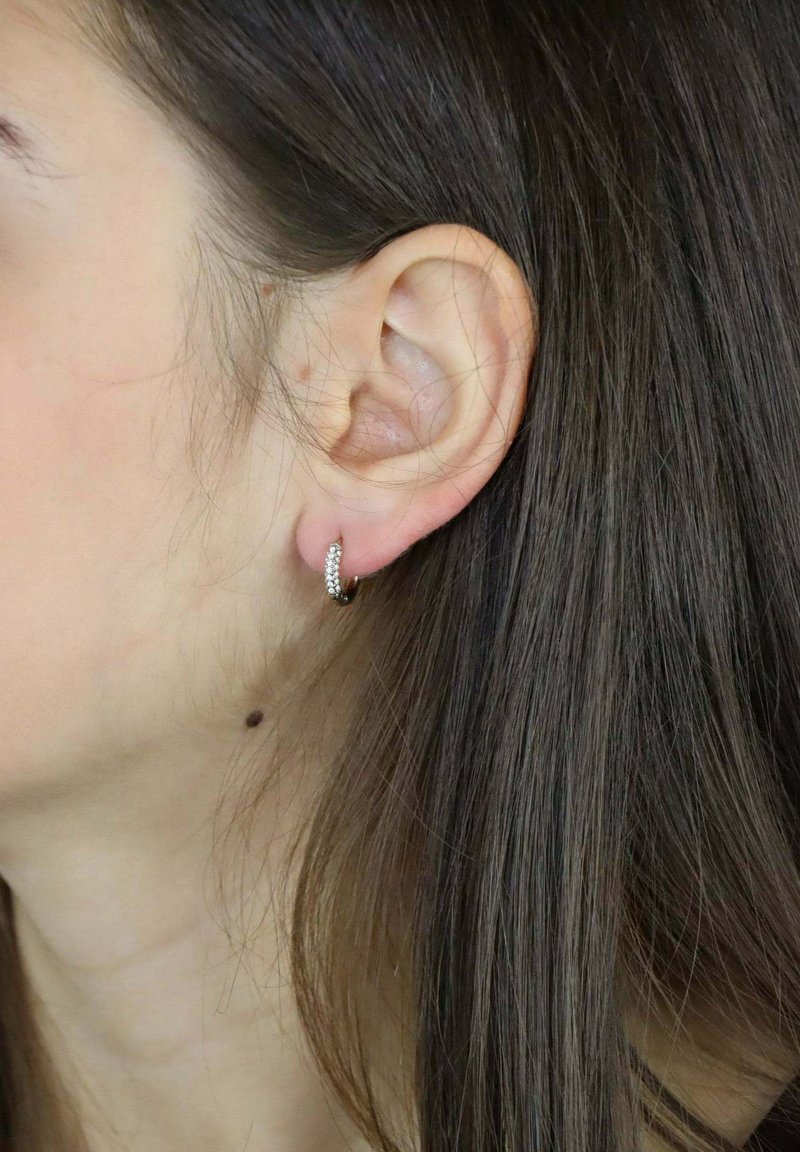 Orecchini a cerchio in argento con piccole pietre preziose bianche, forma rotonda, superficie liscia e un design sottile e testurizzato, indossati a un orecchio.