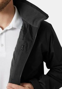 Chaqueta negra con cremallera y cuello forrado de polar, que cuenta con un bolsillo en el pecho con cremallera y una textura suave. La camiseta interior es blanca con botones.