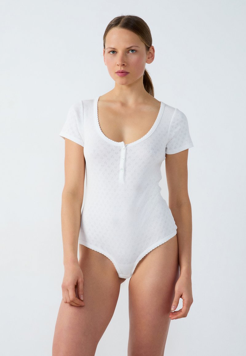 Bodysuit blanco de manga corta con escote redondeado, patrón texturizado y cierre de botones en la parte frontal. Detalle de puntilla en los bordes.