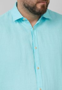 Lichtblauwe linnen shirt met een kraag, knopen aan de voorkant en een licht gestructureerd oppervlak. De knopen zijn licht van kleur en rond.