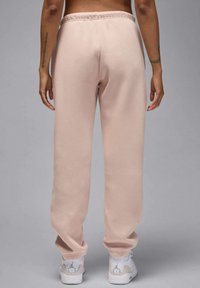 Różowe spodnie dresowe o luźnym kroju, z elastycznym pasem i ściągaczami przy kostkach, w połączeniu z białymi trampkami. Minimalistyczny design i gładka faktura.