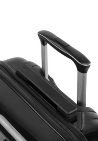 Maleta rodante negra con una superficie lisa, mango metálico retráctil y apertura con cremallera. El mango cuenta con un agarre de goma.