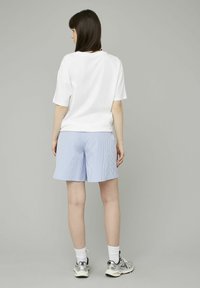 Chemise blanche à manches courtes avec une coupe décontractée, assortie à un short à rayures bleu clair. Le modèle porte des baskets argentées et des chaussettes blanches mi-hautes.