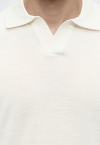 Gros plan d'une personne portant un polo en maille blanche avec un col plat et une encoche en forme de V au niveau de l'encolure.