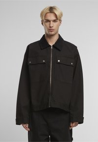 Czarna krótka kurtka z kordurowym kołnierzem, dwoma przednimi kieszeniami i srebrnymi okuciami. Posiada zamek błyskawiczny i gładką fakturę.