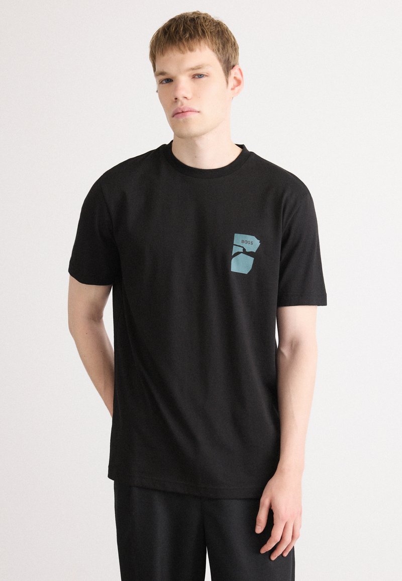 Zwarte T-shirt van katoen met een ronde hals, met een blauw grafisch logo op de linkerborst. Korte mouwen en een relaxed fit.