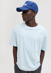 Lichtblauw T-shirt met korte mouwen van zachte katoenen stof, met een relaxte pasvorm. Gecombineerd met een navy pet met witte letters.