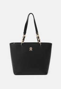 Black leather tote bag with two handles, gold-tone chain accents, and a logo on the front. Smooth texture and structured design.