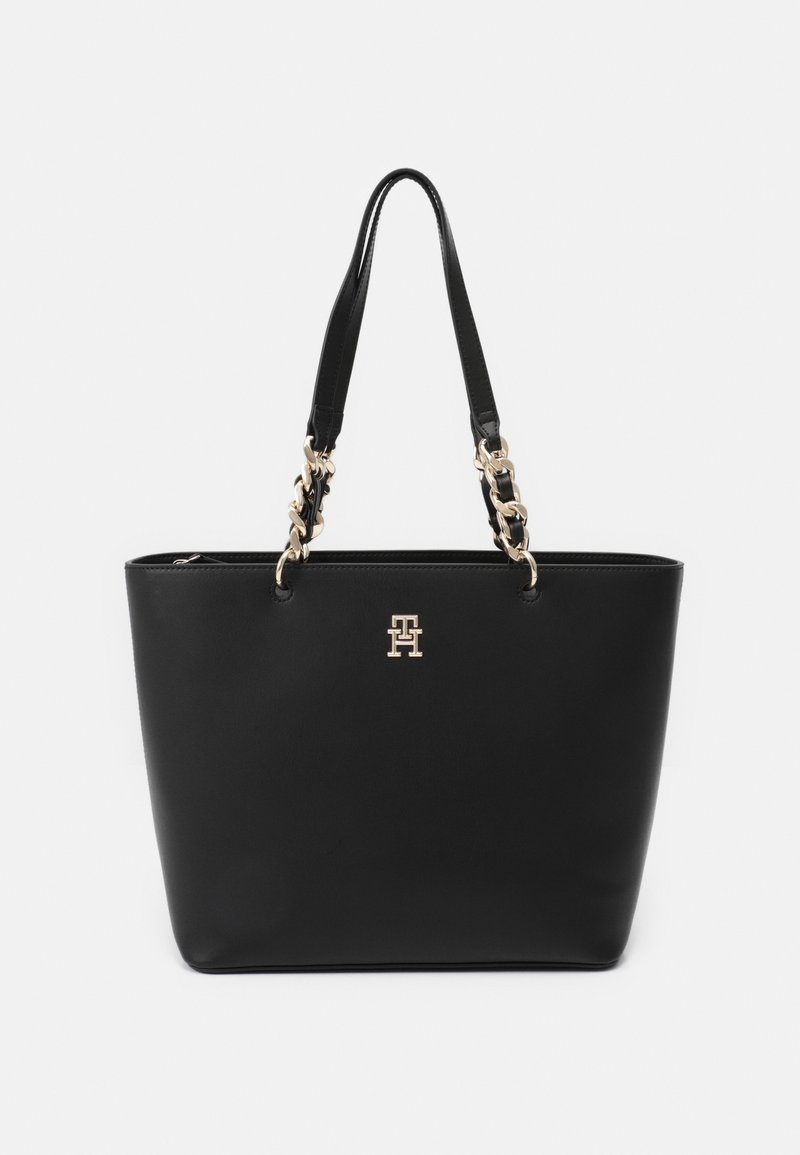 Black leather tote bag with two handles, gold-tone chain accents, and a logo on the front. Smooth texture and structured design.