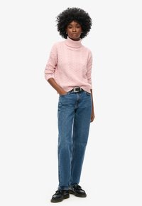 Roze kabelgebreide coltrui, gecombineerd met blauwe recht-pas jeans en zwarte schoenen, heeft lange mouwen en een ontspannen pasvorm.