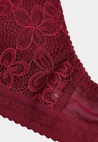 Burgundy lace bralette featuring floral patterns, textured fabric, and a ribbed band with subtle detailing. Elegant and intricate design.