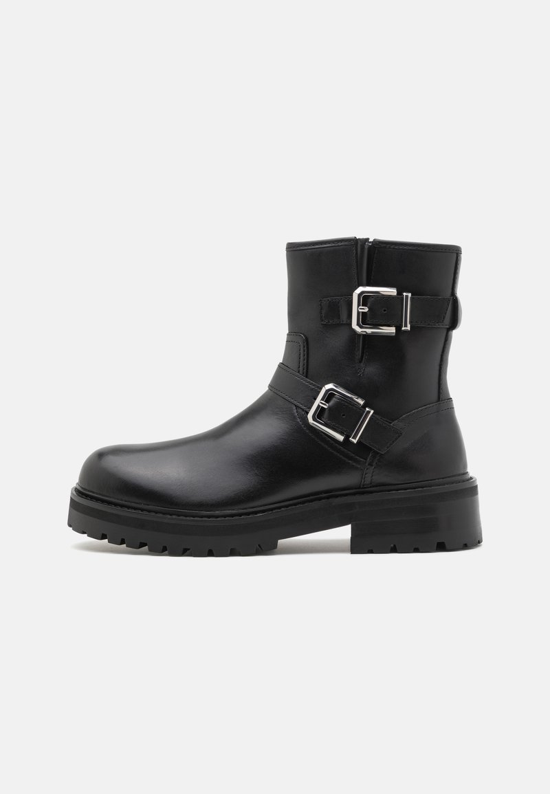Black leather ankle boot with two silver buckles, rounded toe, and a thick rubber sole with traction. Smooth texture with minimal design.