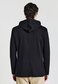 Schwarze Kapuzenjacke mit glatter Textur, taillierter Passform und belüftetem Rücken, seitlichen Taschen und sauberen Nähdetails.