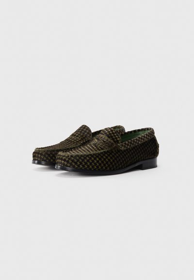 Pareja de mocasines de hombre en patrón de espiga marrón y negro, con tacones bajos negros y un forro interior verde, sobre un fondo blanco liso.