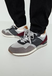 Graue und schwarze Sneaker aus Wildleder- und Mesh-Materialien. Mit burgunderroten Akzenten und weißen Schnürsenkeln. Gummisohle mit strukturiertem Profil.