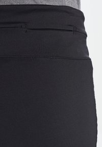 Czorna sportowa spódniczka z gładkiego, elastycznego materiału. Posiada wysoki pas i minimalne szwy, widok z boku.