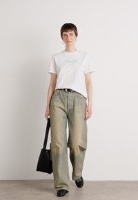 Hvit T-skjorte med lys blå "Calvin Klein" logo, løse lysegrønne jeans, svart belte og svart håndveske, brukt med svarte sko.