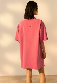 Oversized kortearmige jurk van helder roze katoen. Kenmerkt zich door een ronde halslijn, onafgewerkte zoom en een relaxte pasvorm. Licht gestructureerd oppervlak.