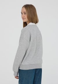 Szary sweatshirt z białym kołnierzykiem, charakteryzujący się luźnym krojem i długimi rękawami. Materiał wydaje się miękki o gładkiej fakturze.