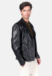 Czarna skórzana kurtka motocyklowa z pikowanymi akcentami na ramionach i rękawach, zamkami błyskawicznymi w kieszeniach oraz kołnierzem z klapami, wykonana w dopasowanej sylwetce.