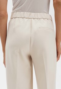 Beige broek gemaakt van gladde stof, met een elastische tailleband en één opgestikt achterzakje. Tailored fit.