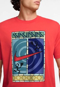 Camiseta de algodón roja con un gráfico central que presenta paneles azules y verdes, un gran logo de Nike y figuras de palo jugando deportes de raqueta.