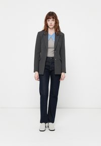 Blazer grigio su misura con due bottoni, revers a scaldino, abbinato a un top grigio a coste e jeans in denim scuro. Calzature sono scarpe grigie chiare.