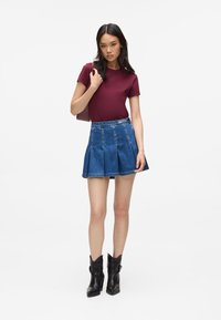 Tricou bordeaux, asortat cu o fustă din denim albastru, evazată, și cizme negre cu gleznă. Fusta are pliuri și un talie medie.