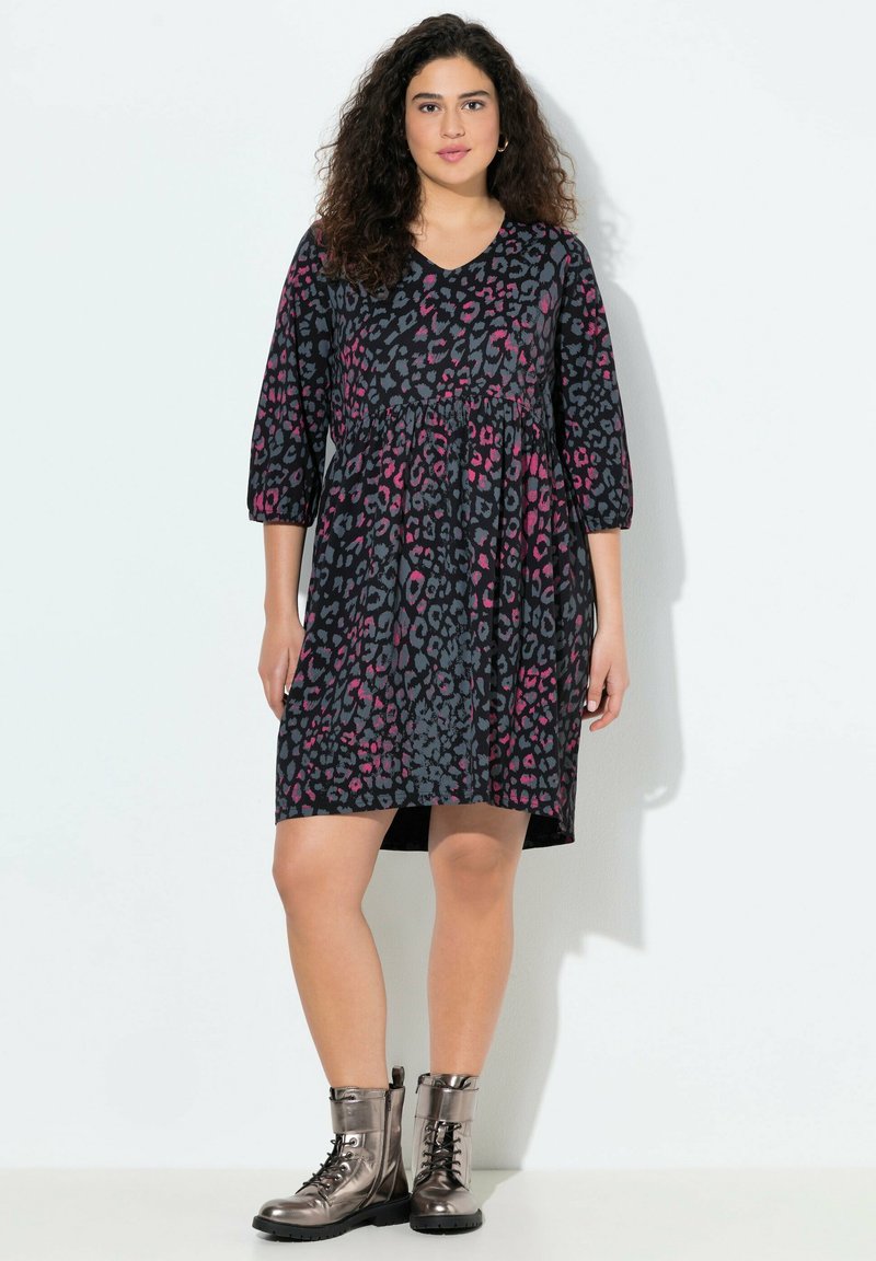 Schwarzes Kleid mit pinkem und grauem Leopardenmuster, V-Ausschnitt, Drei-Viertel-Ärmel, tailliert, kombiniert mit metallisch grauen Kampfstiefeln.